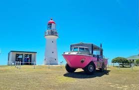 Pink amphibious vehicle and lighthouse on a sunny day.