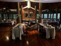 Wooden-floored wedding reception venue with round tables dressed in white and sage green linens, with large windows and a fireplace.