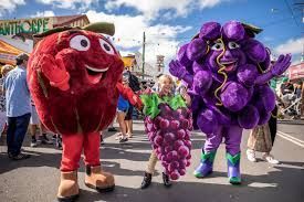 Apple and grape mascots with a girl posing at a festival, bright colors and smiling expressions.