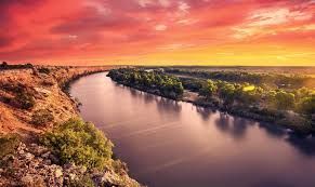 A river flowing through a valley surrounded by trees at sunset.