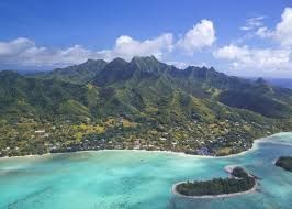 An aerial view of a small island in the middle of the ocean with mountains in the background.