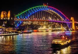 Sydney Harbour Bridge illuminated with rainbow colors at night, a boat on the water.