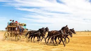 Stagecoach pulled by four horses racing across a dusty plain under a blue sky.
