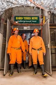 Miners in orange coveralls emerge from the Hard Times Mine entrance.
