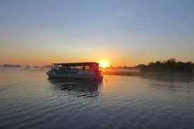 Boat on calm water at sunrise; orange sky, silhouettes of trees, and mist.