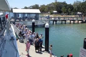 A group of people are standing on a dock next to a body of water.