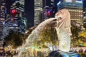 Merlion statue spouting water in Singapore, with city skyline at night.