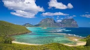 People wading in turquoise water with mountains in the background, Lord Howe Island, Australia.