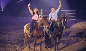 A man and a woman are riding horses in a rodeo arena.