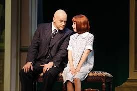 A man and a little girl are sitting on a bench on a stage.