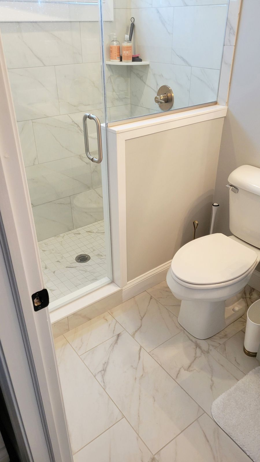 Bathroom with a marble tiled floor, a glass shower, and a white toilet.