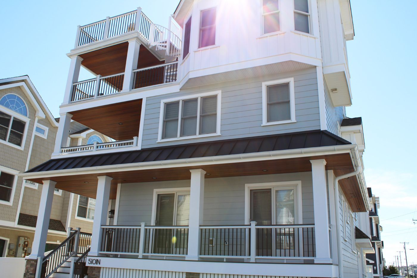 A multi-story beach house with a light blue exterior, multiple balconies, and a sunny sky.
