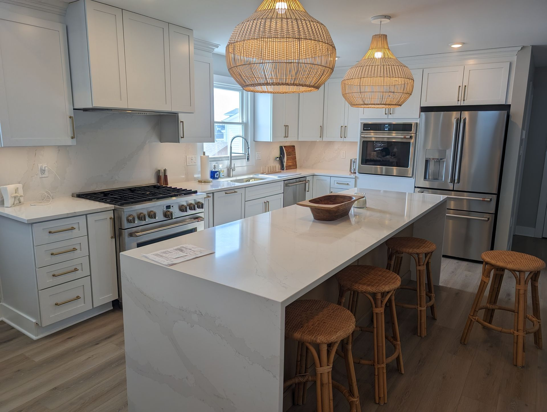 Bright, modern kitchen with white cabinets, island with stools, stainless steel appliances, and woven light fixtures.