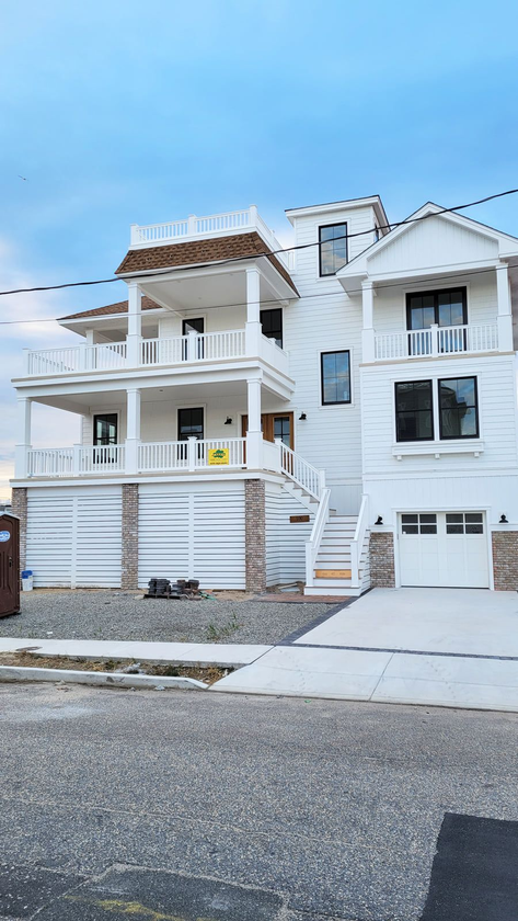 White beach house with multiple levels and balconies, built above ground level with stone siding and a driveway.