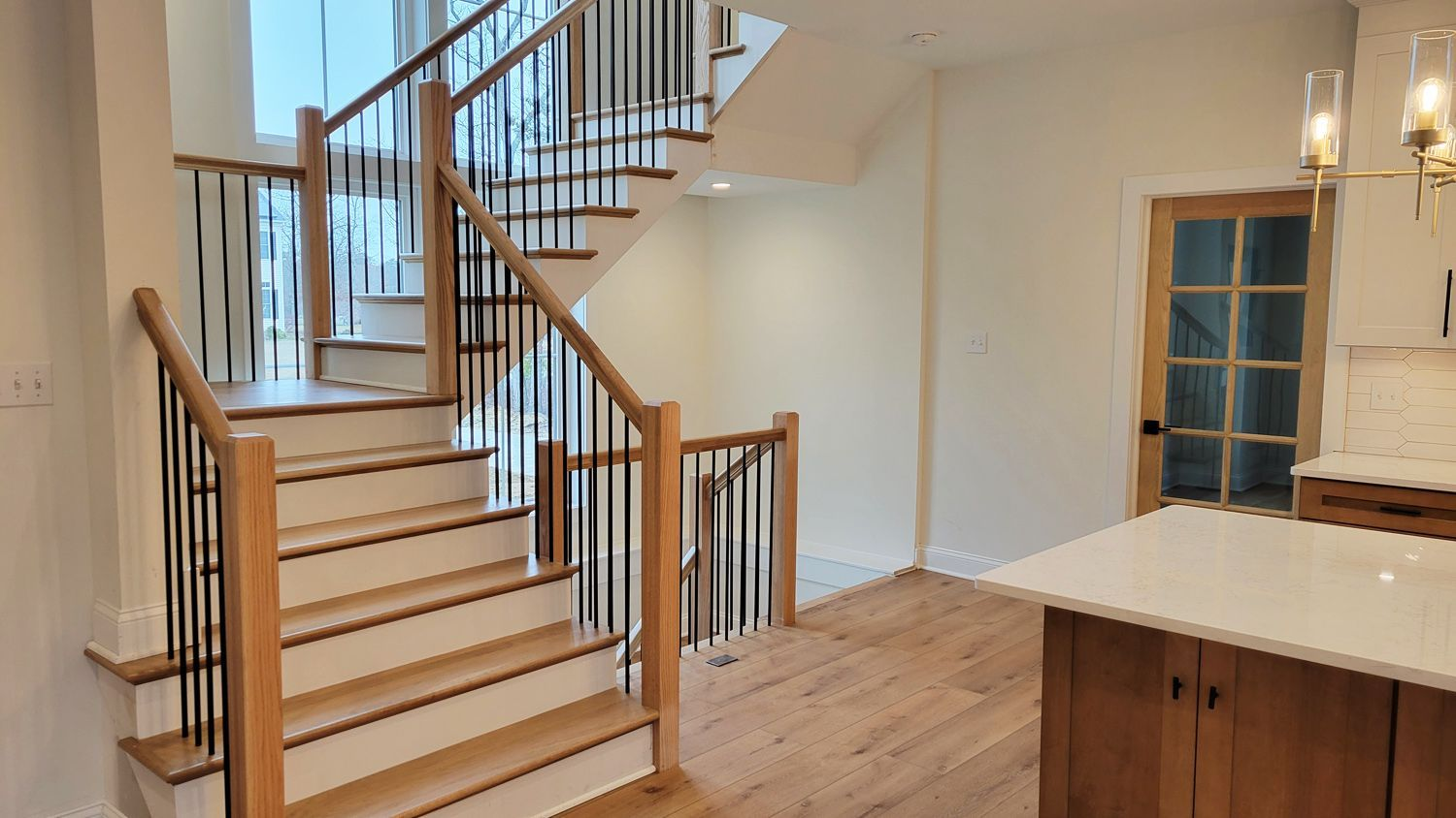 A staircase with light wood steps and railing, black spindles, and white walls. The stairs lead to an upper level.