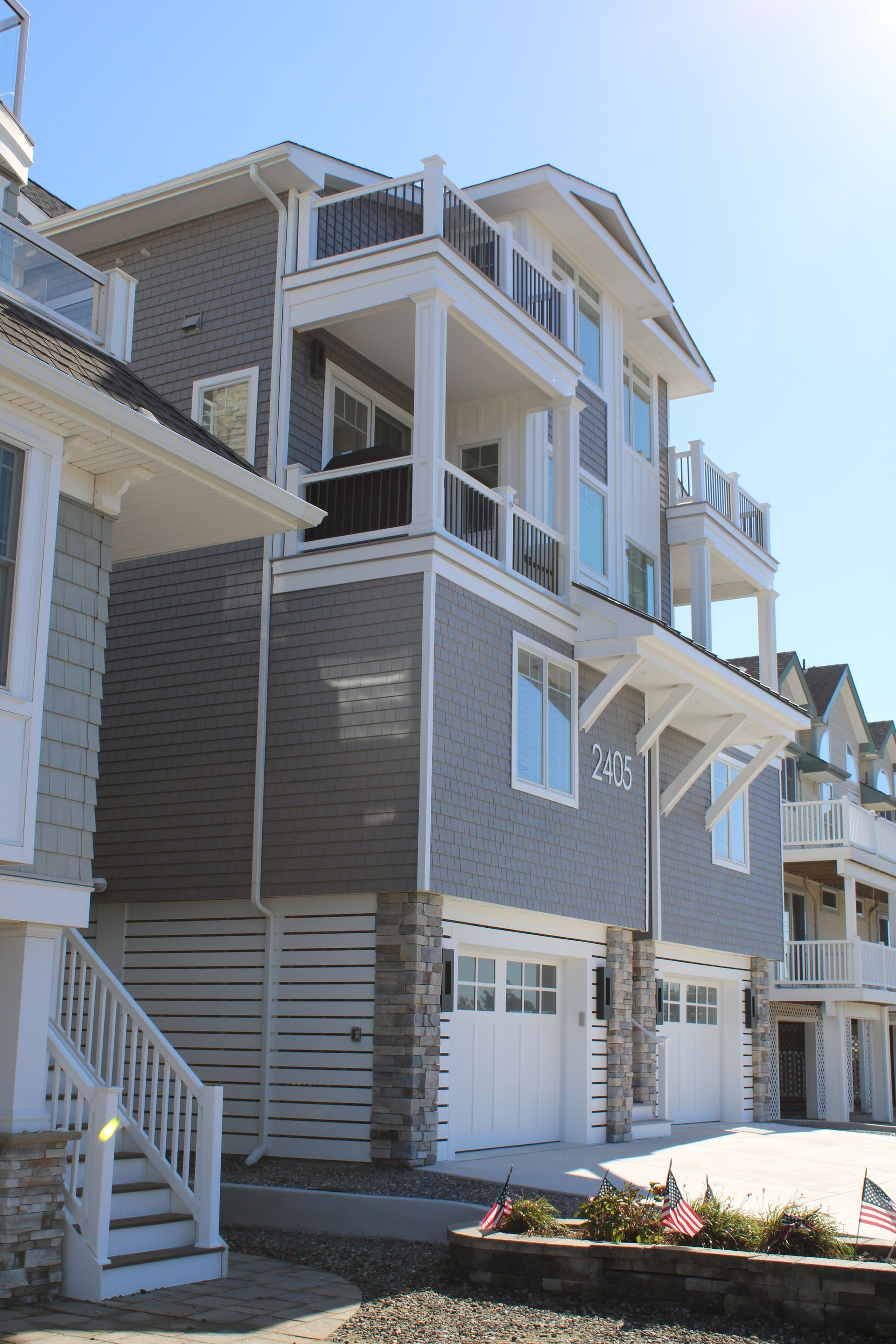 Multi-story gray beach house with balconies and white garage doors under a blue sky.