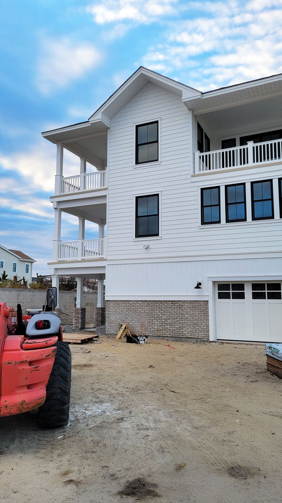 White house under construction with balconies. A red construction vehicle is in the foreground. Cloudy sky in the background.