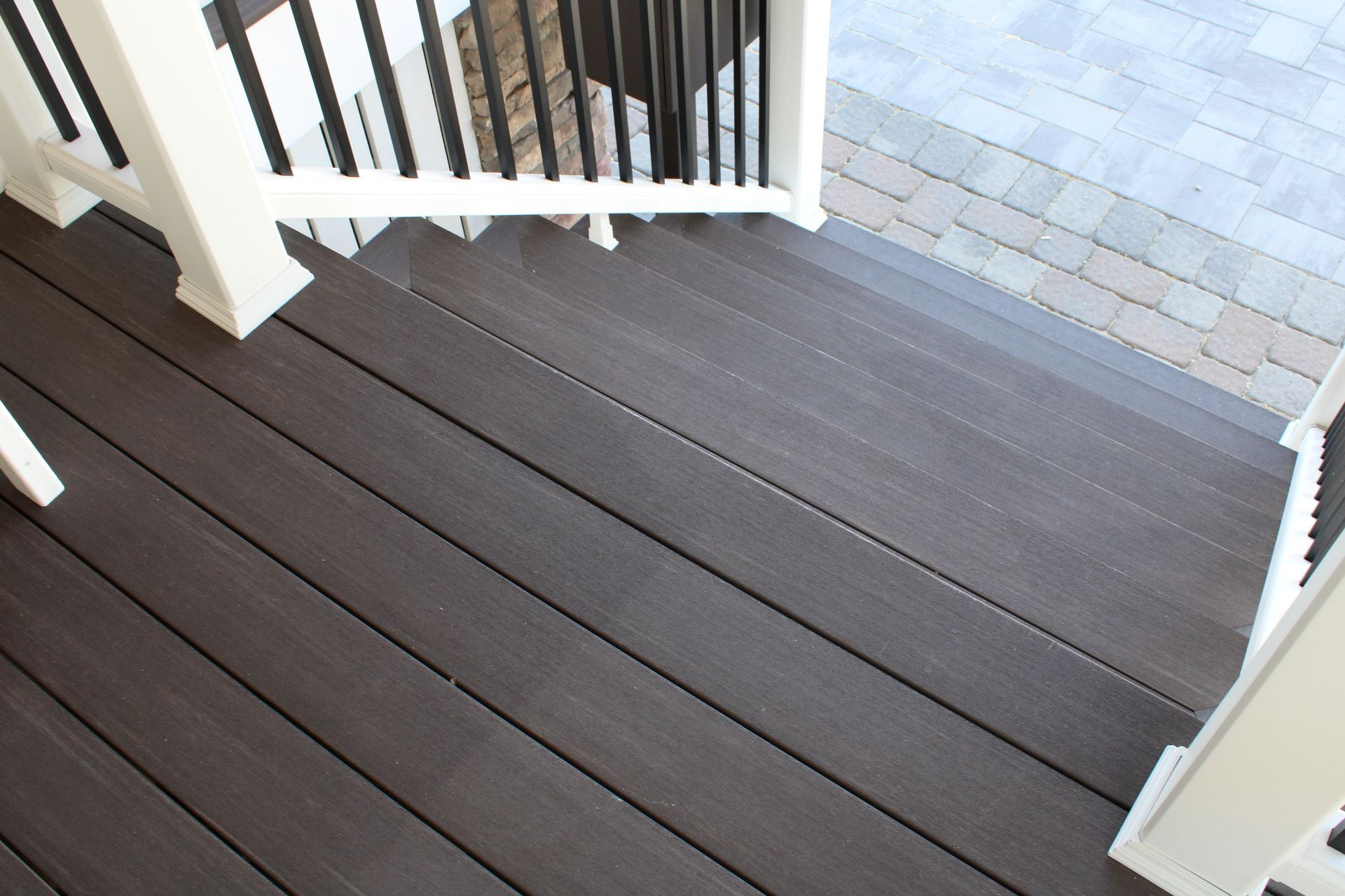 Dark gray composite deck with white railing; stairs leading down to a patterned brick patio.