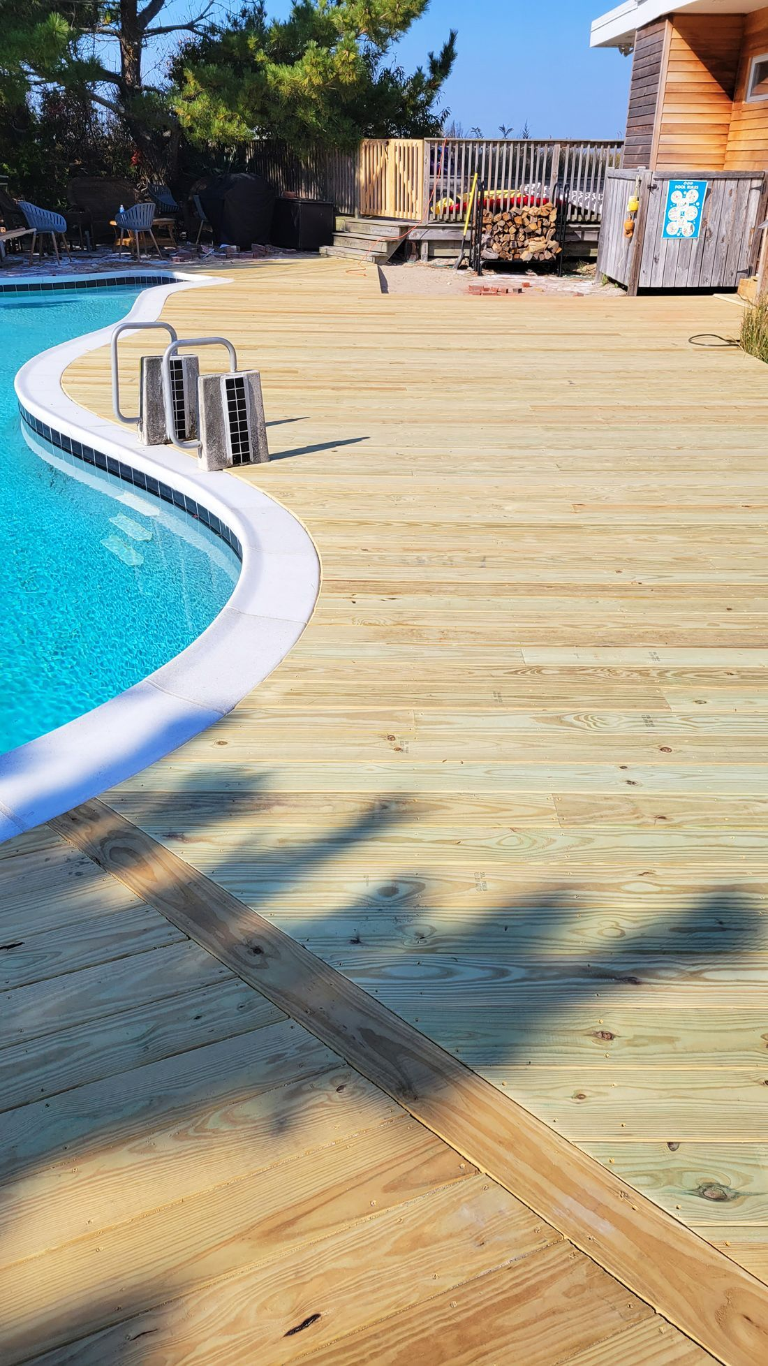 Poolside wooden deck with curved edge and turquoise water. Wooden beams and structure in the background.