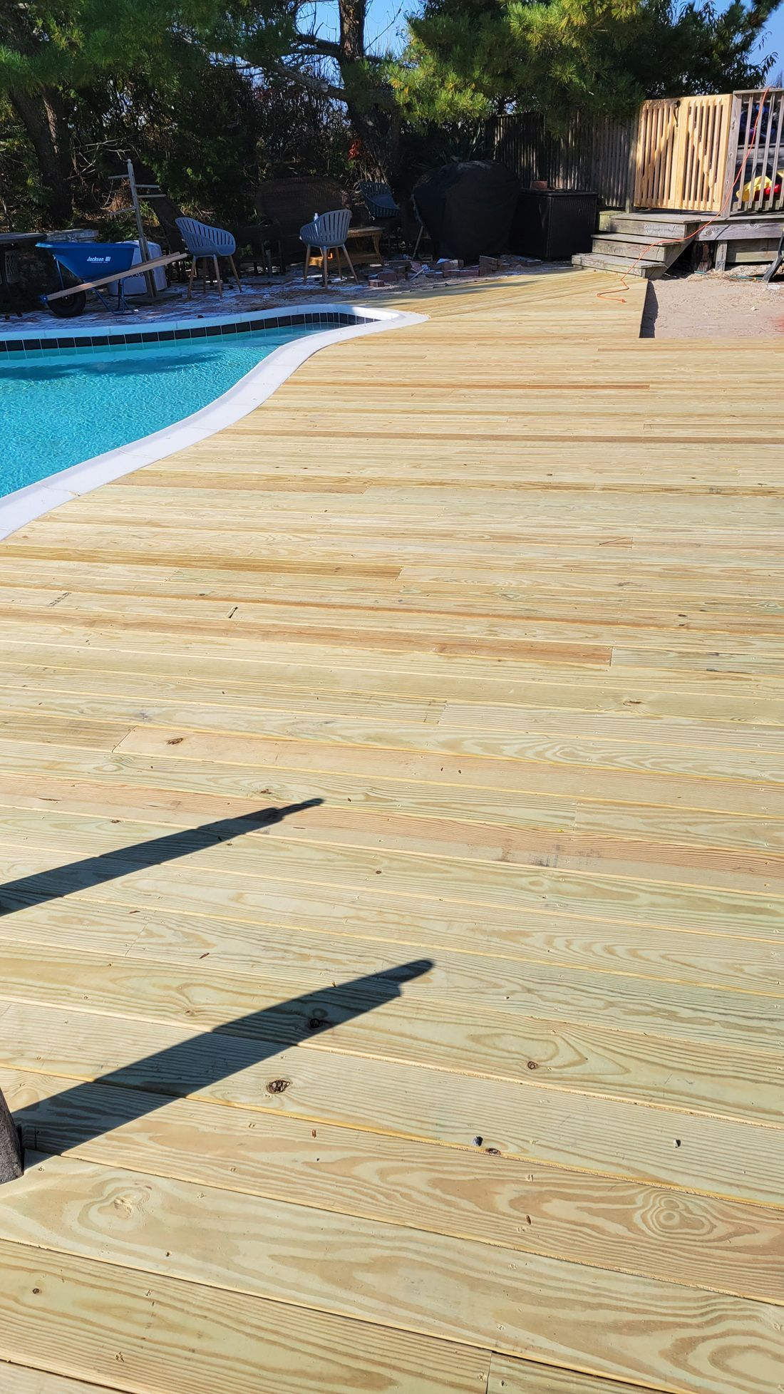 Wooden deck surrounds a pool, with clear water and a bright sky above.