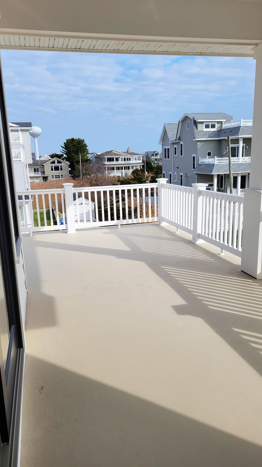 A sunny outdoor deck with white railings, overlooking buildings and a water tower. The sky is blue with scattered clouds.