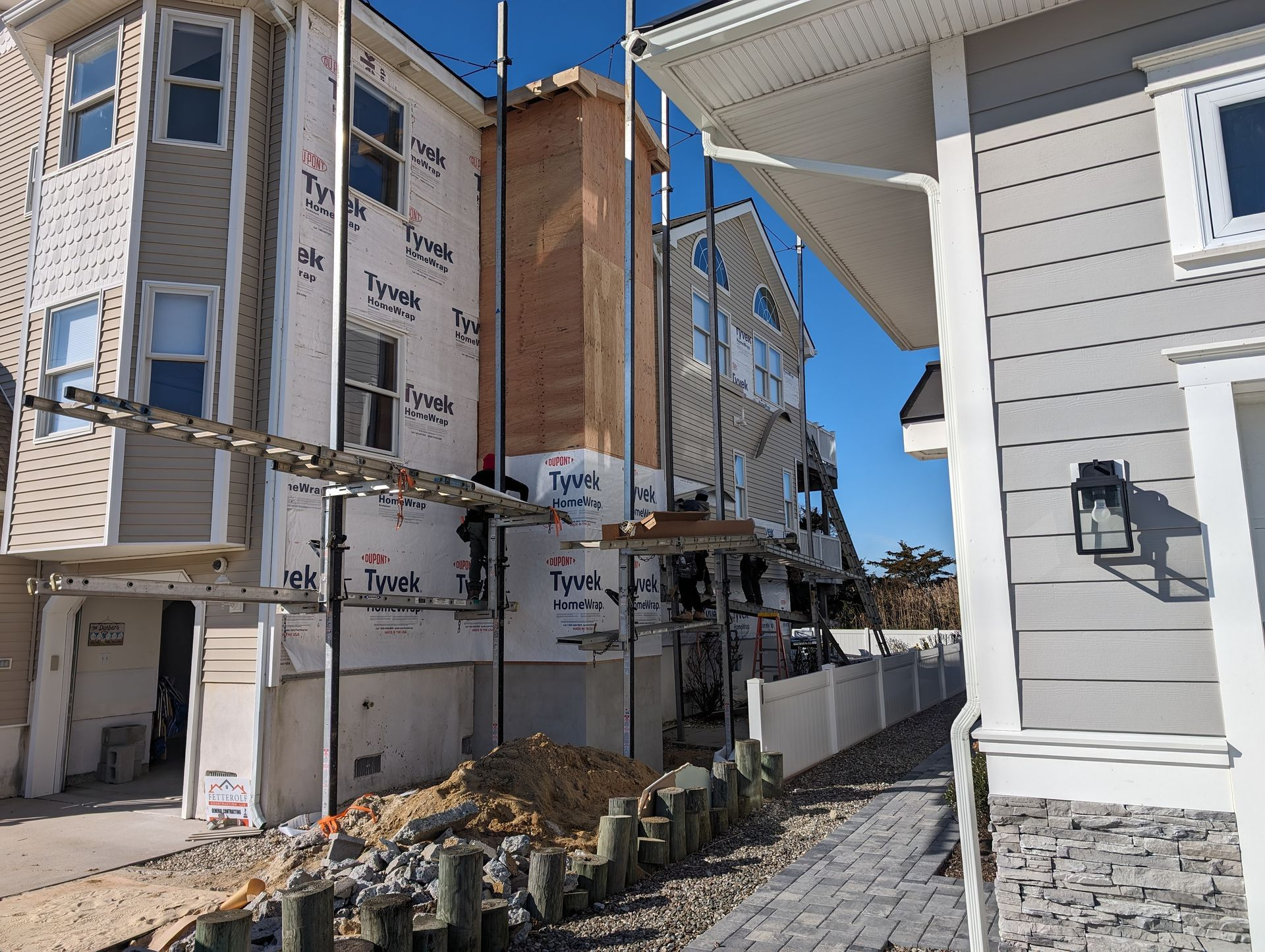 Construction site with multi-story buildings; scaffolding surrounds a brick chimney. Bright blue sky.