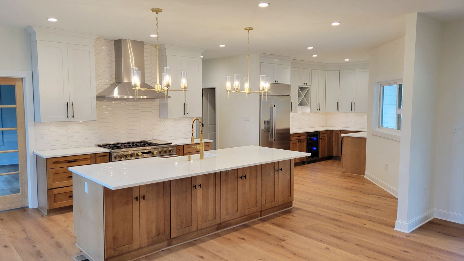 Spacious kitchen with light wood floors, white countertops, and wood and white cabinets. Gold fixtures and a large island add to the modern design.