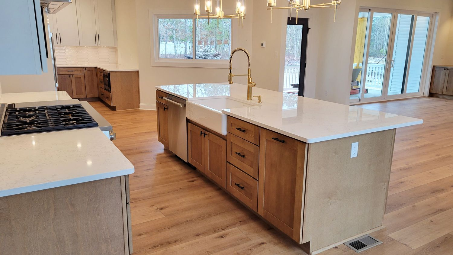 Newly constructed kitchen with light wood cabinets, white countertops, and gold accents. An island features a sink and faucet.