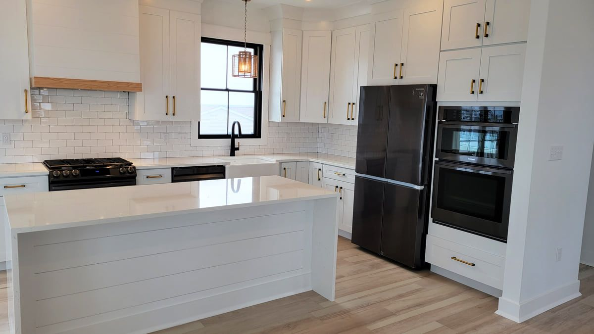 White kitchen with island, cabinets, and stainless steel appliances. Natural light from window.