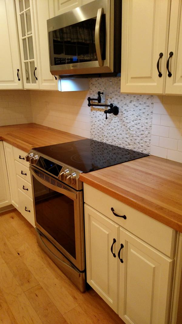 Kitchen with white cabinets, wooden countertops, and a stainless steel stove. A microwave is mounted above the stove.