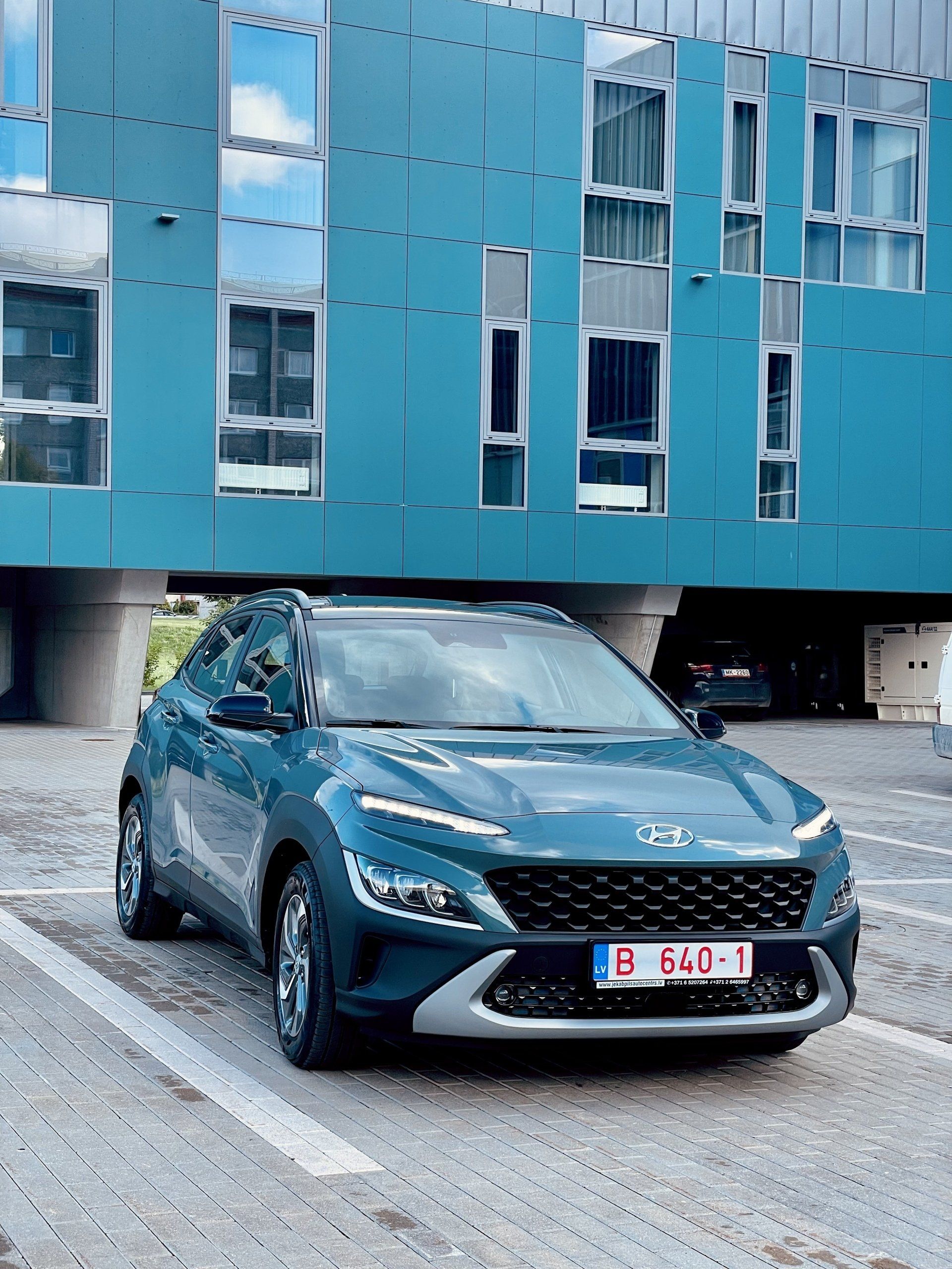 Zila automašīna ir novietota pie zilas ēkas.