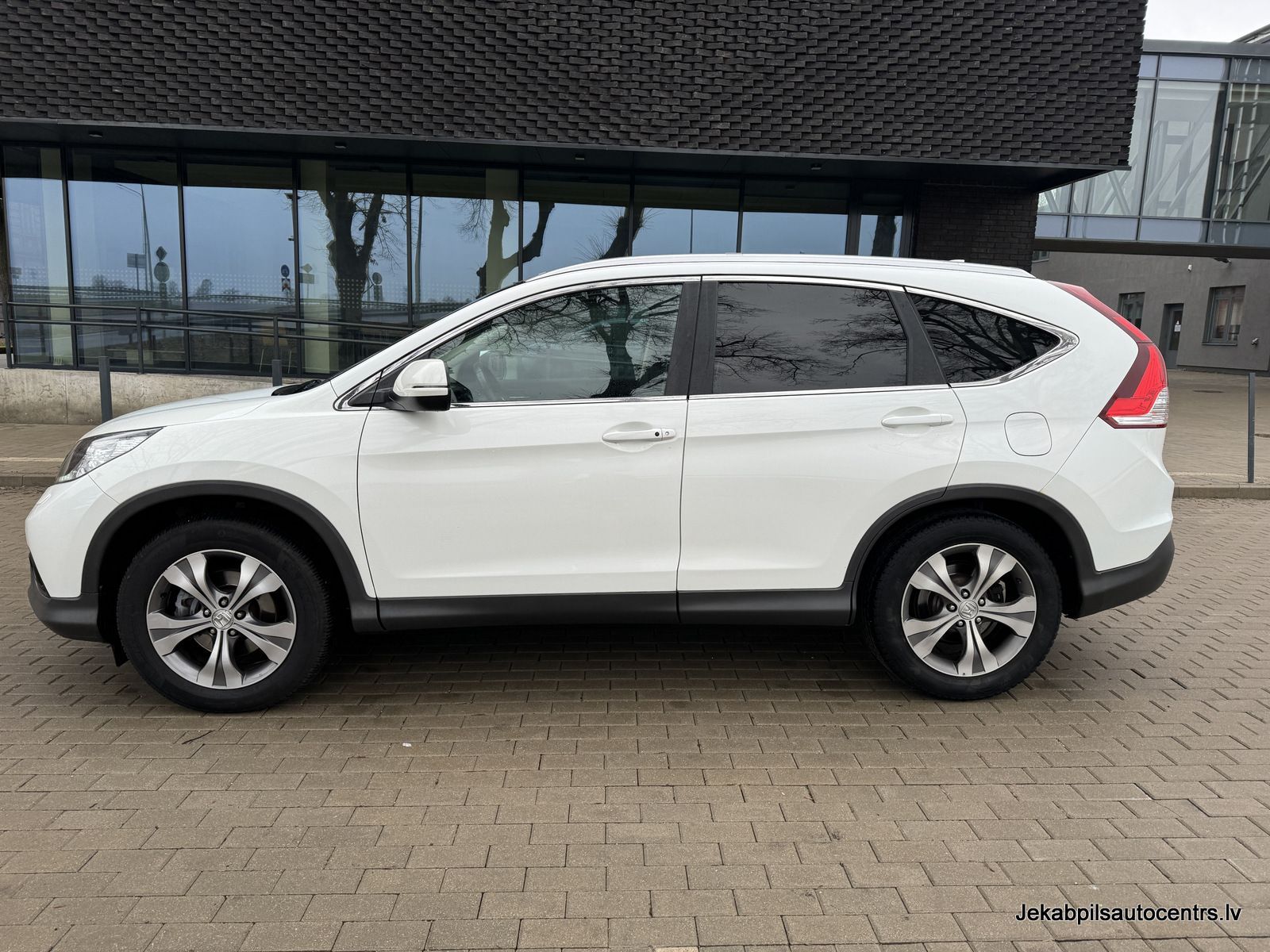 Balta honda cr v ir novietota uz ķieģeļu ietves ēkas priekšā.