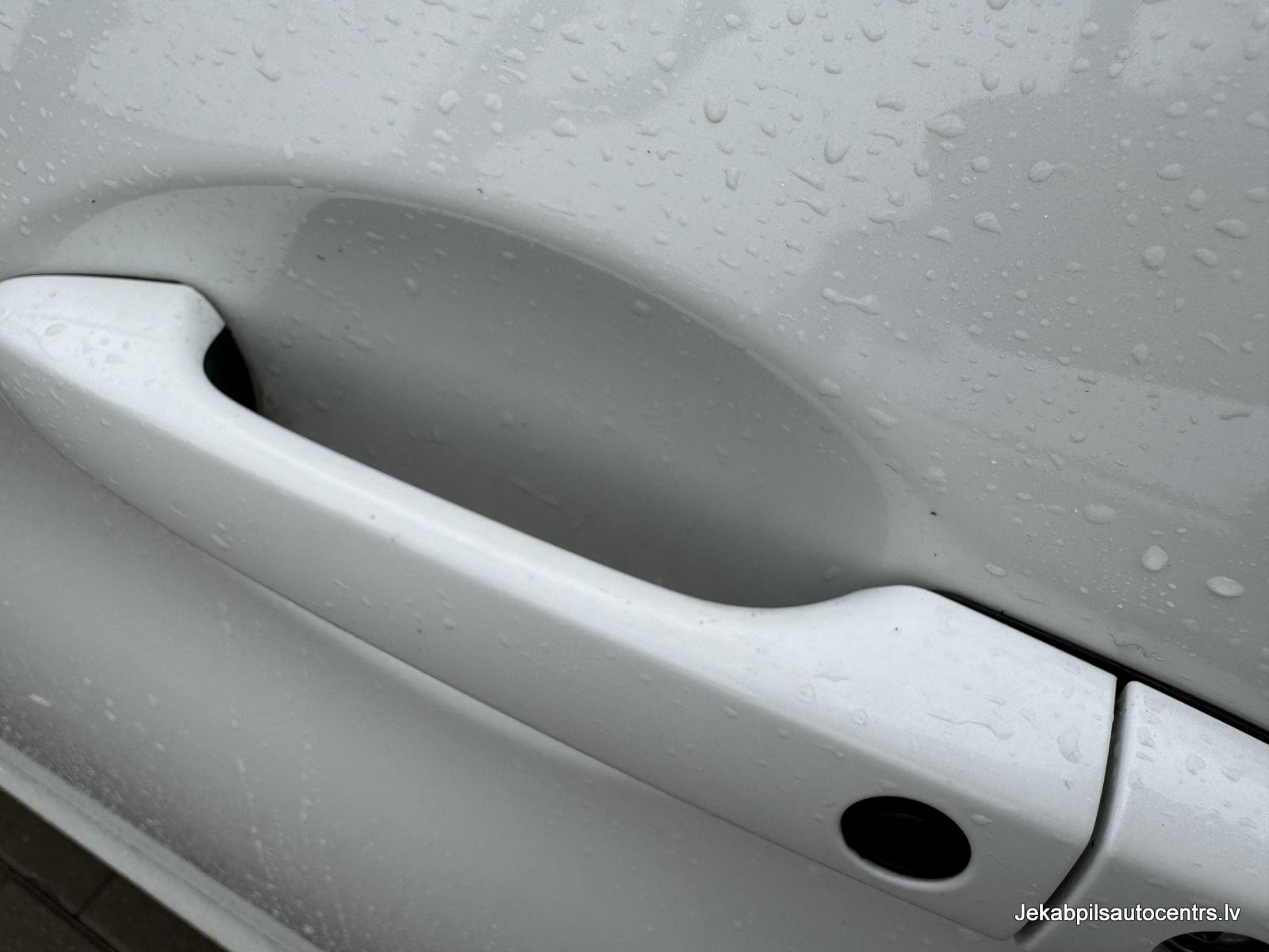 Tuvplāns ar baltu automašīnas durvju rokturi