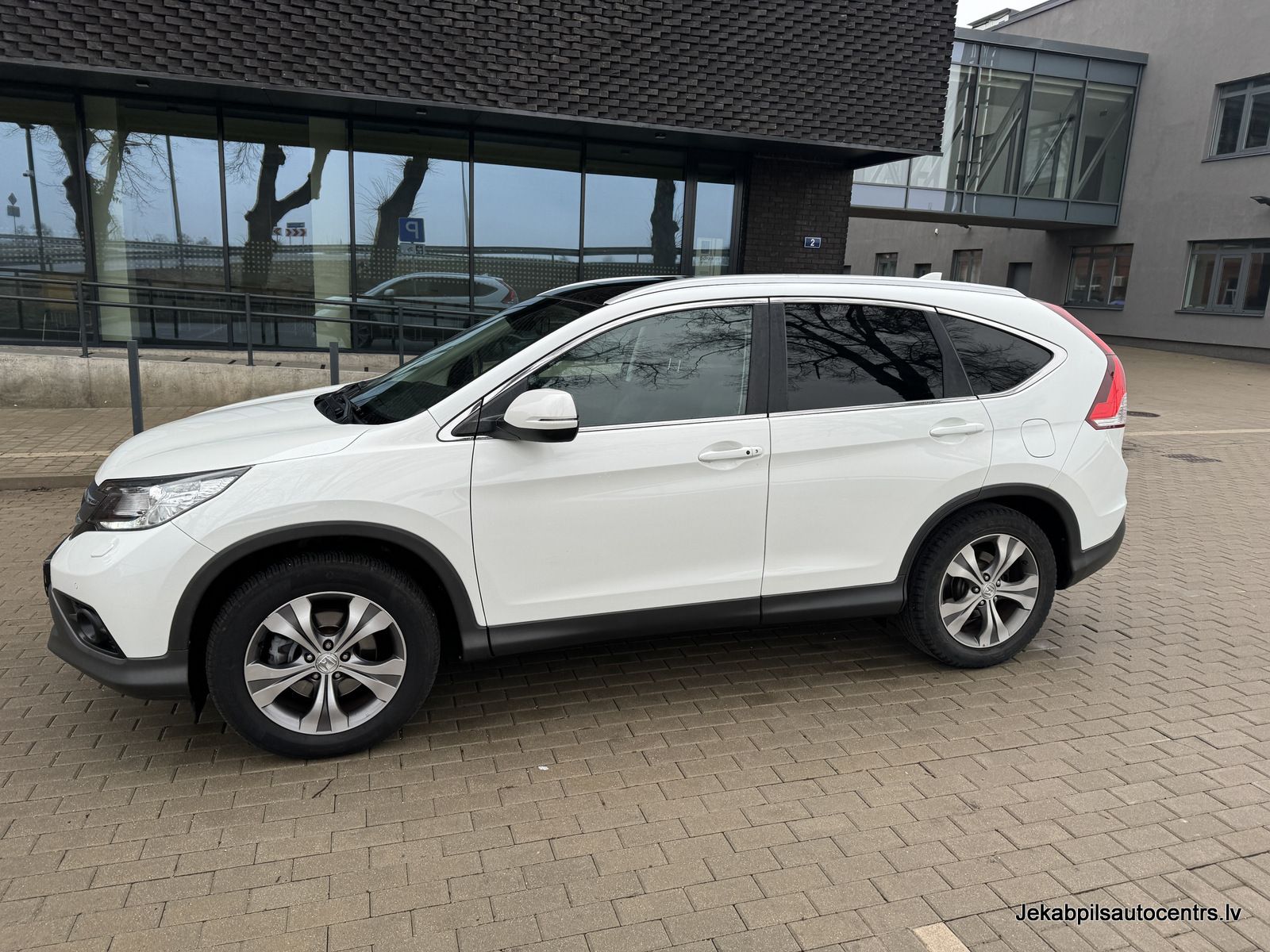 Balta honda cr v ir novietota pie ēkas.