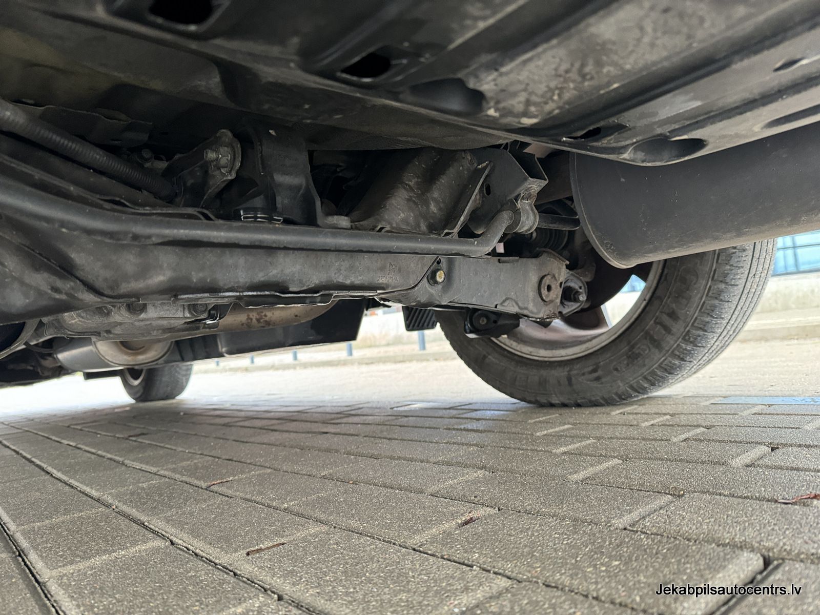 Automašīnas apakšdaļa ir parādīta uz ķieģeļu ietves.