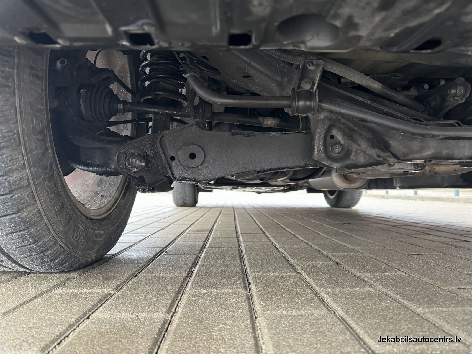 Automašīnas apakšdaļa ir parādīta uz ķieģeļu bruģa.