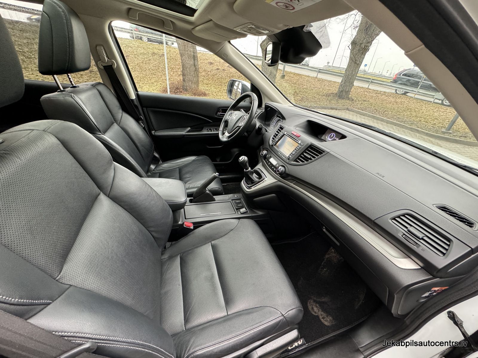 Automašīnas salons ar melniem ādas sēdekļiem un instrumentu paneli.