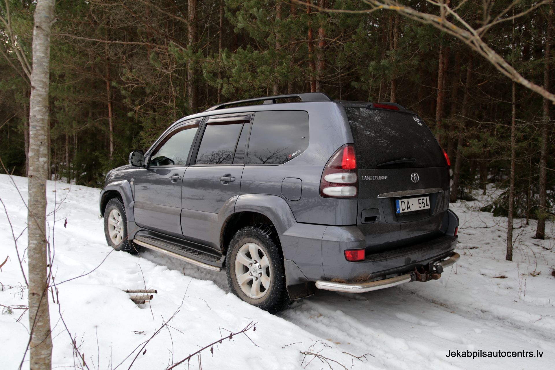 Uz sniegota ceļa mežā stāv toyota land cruiser.
