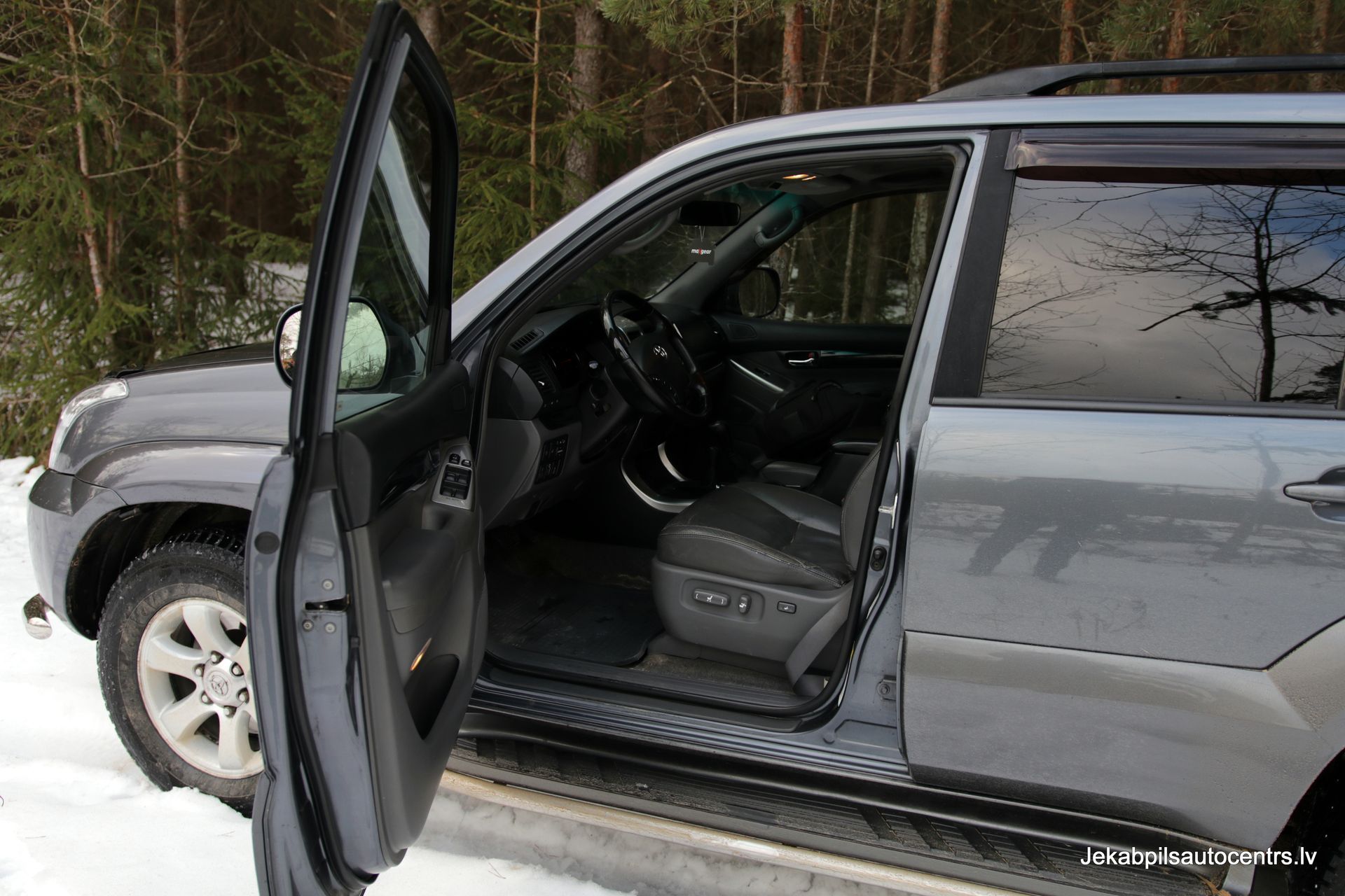 Pelēks apvidus auto ar atvērtām durvīm stāv sniegā.