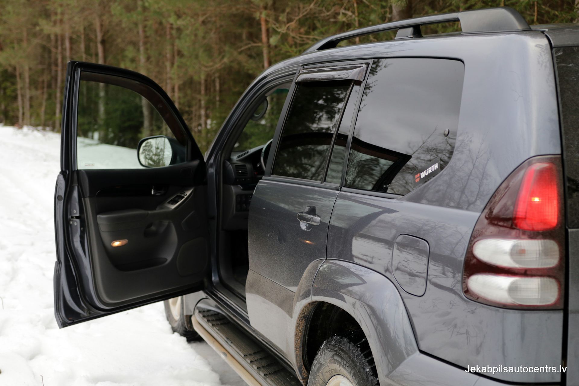 Pelēks apvidus auto stāv sniegā ar atvērtām durvīm.