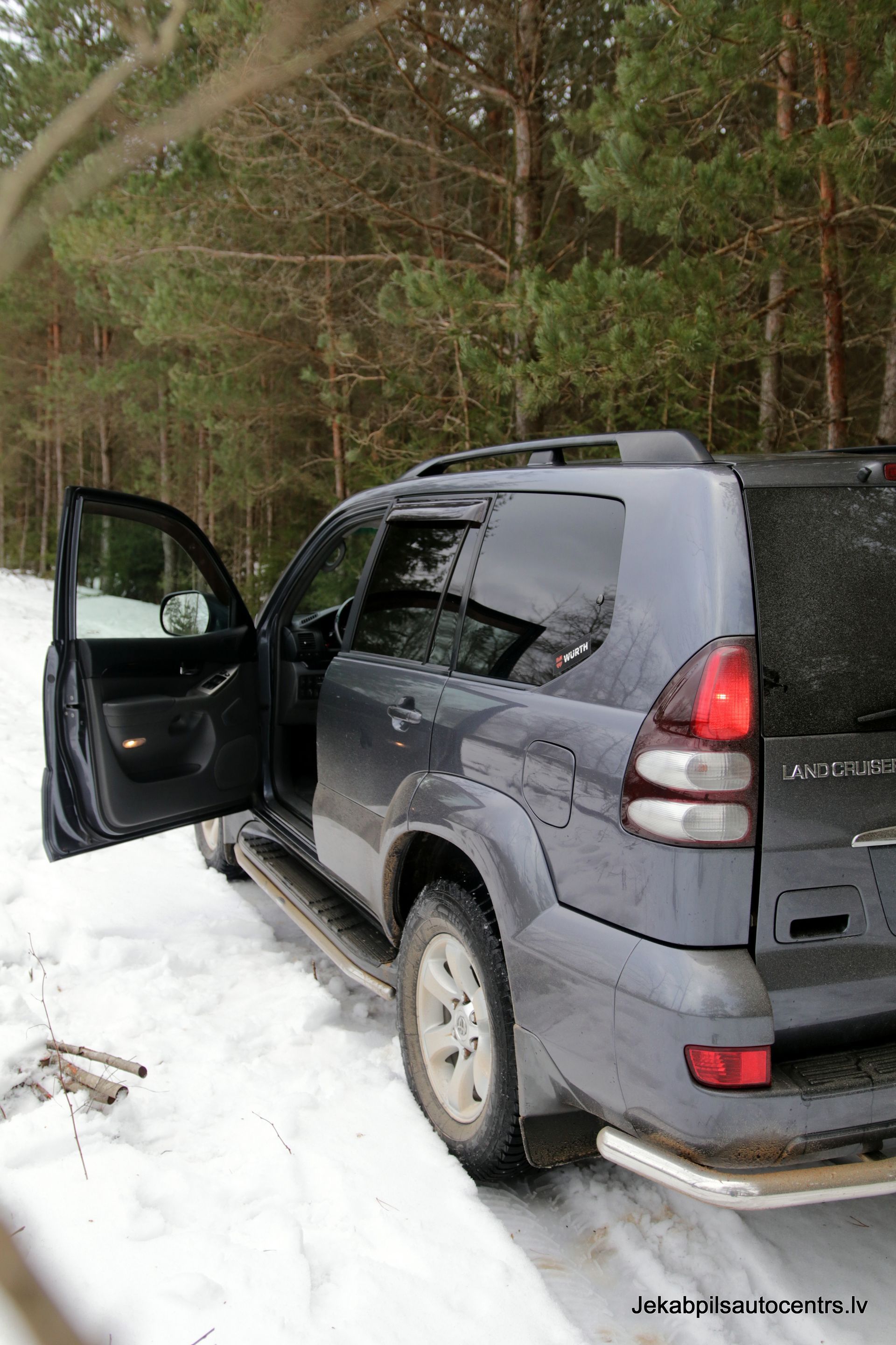 Pelēks apvidus auto ar atvērtām durvīm stāv sniegā.