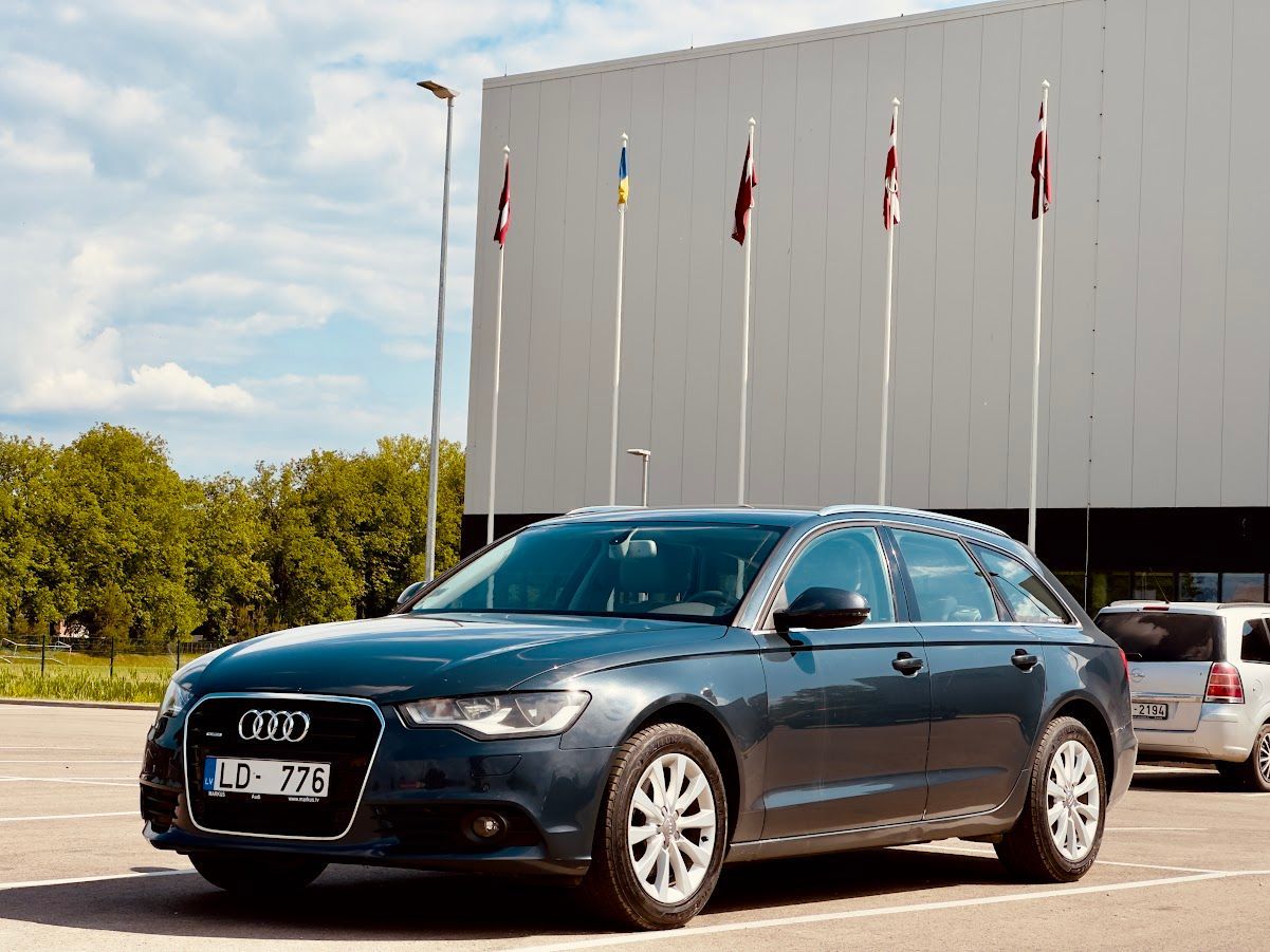 Zils audi ir novietots stāvlaukumā pie ēkas.