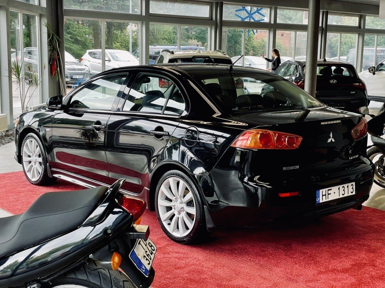 Melna mašīna ir novietota salonā pie motocikla.