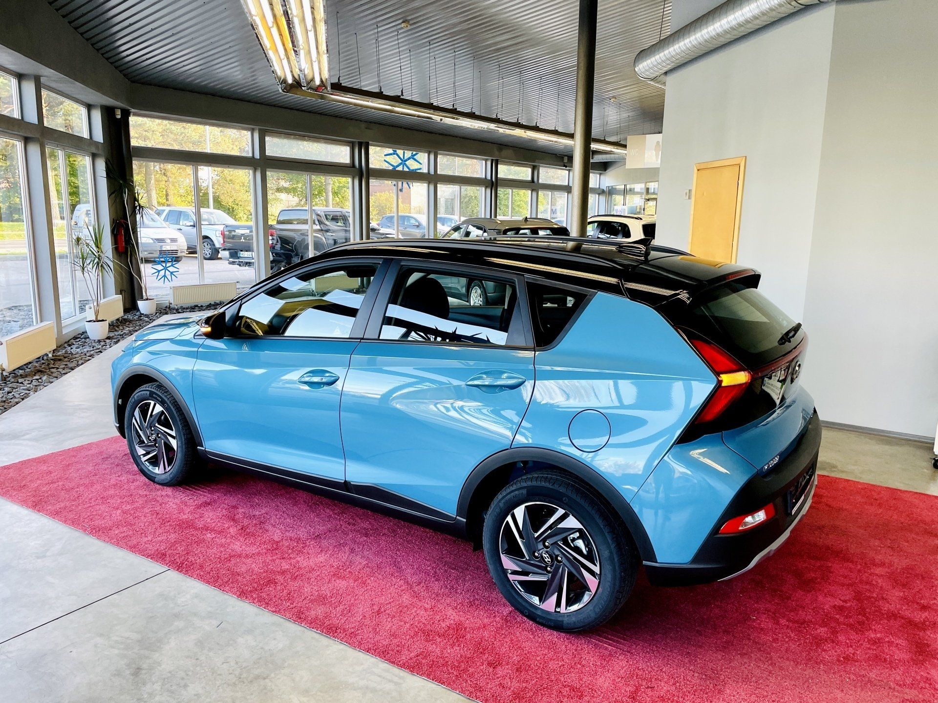 Izstāžu zālē uz sarkana paklāja sēž zila mašīna.