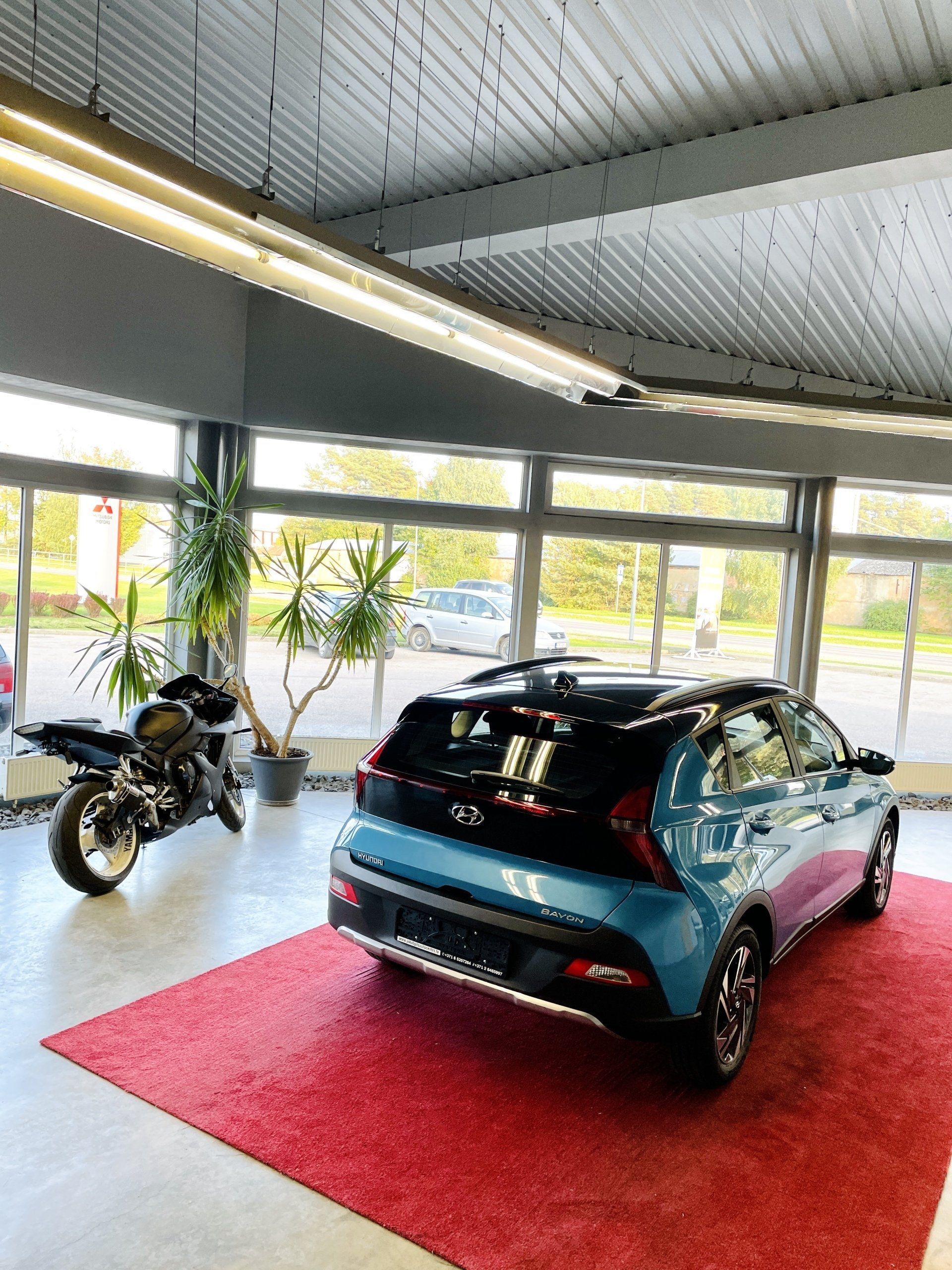 Zila automašīna ir novietota salonā pie motocikla.