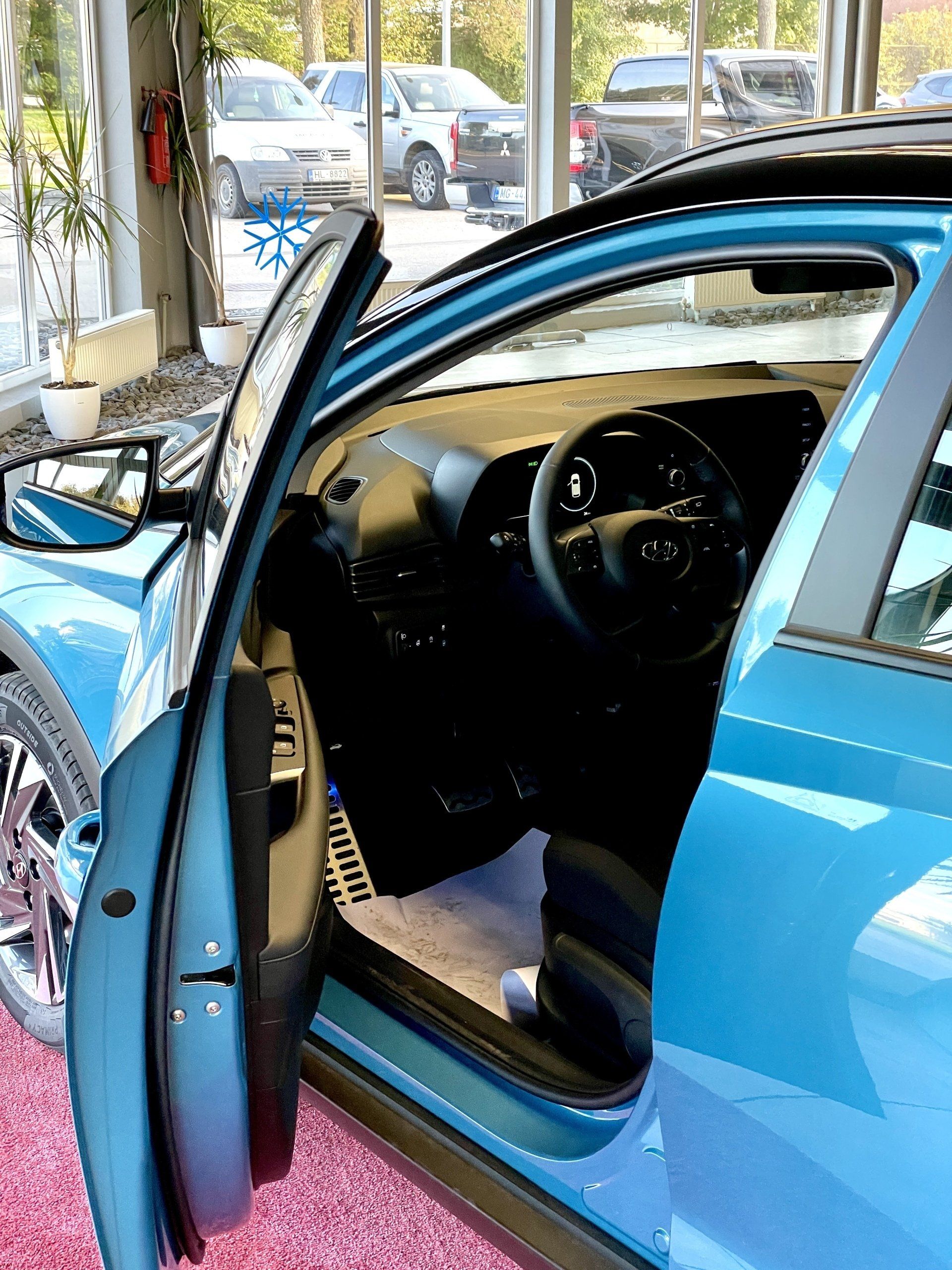 Izstāžu zālē sēž zila mašīna ar atvērtām durvīm.