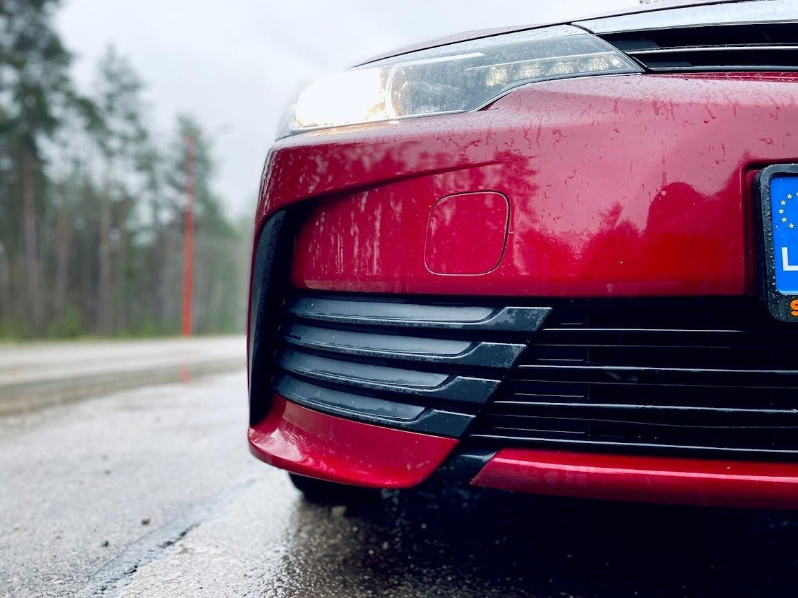 Lietū ceļa malā stāv sarkana mašīna.