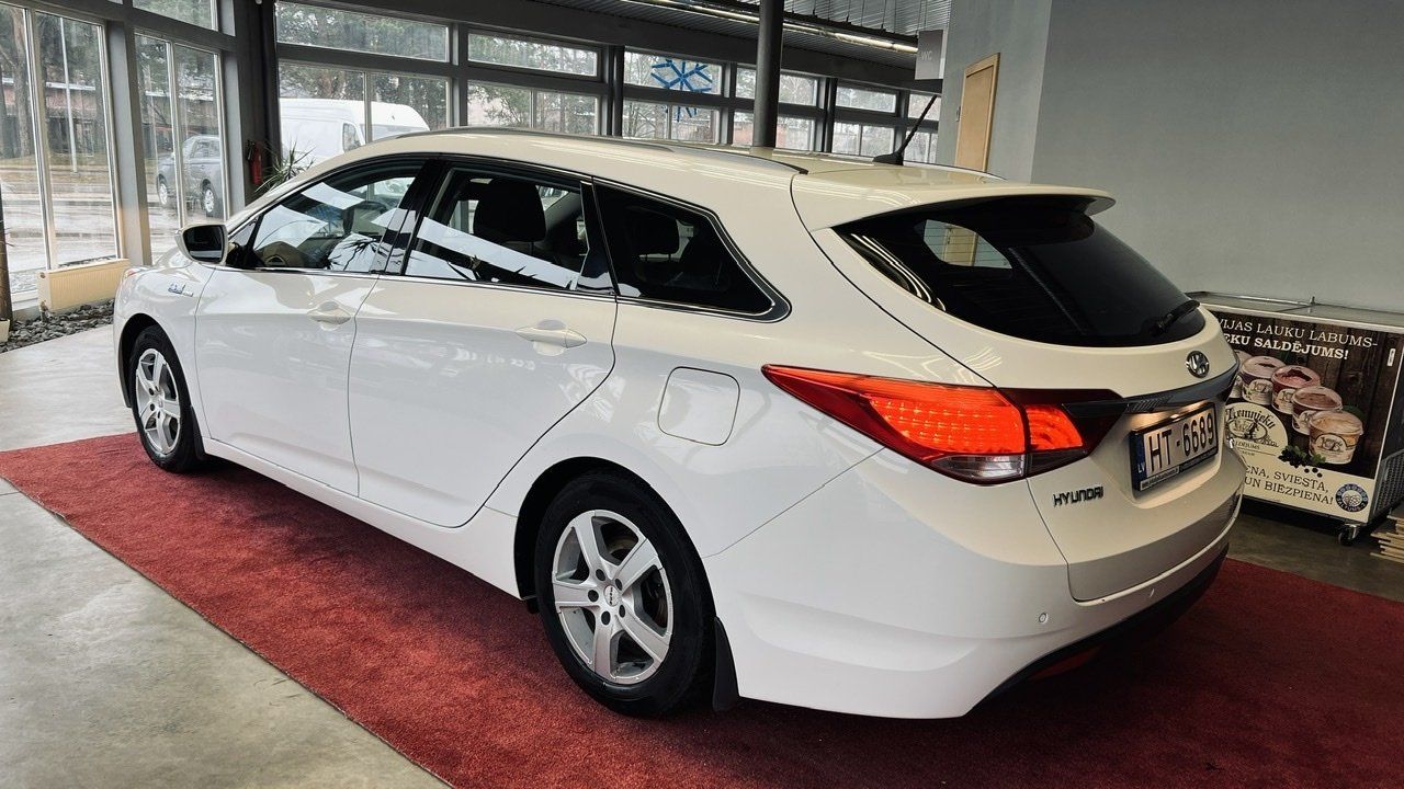 Balta automašīna ir novietota salonā uz sarkana paklāja.