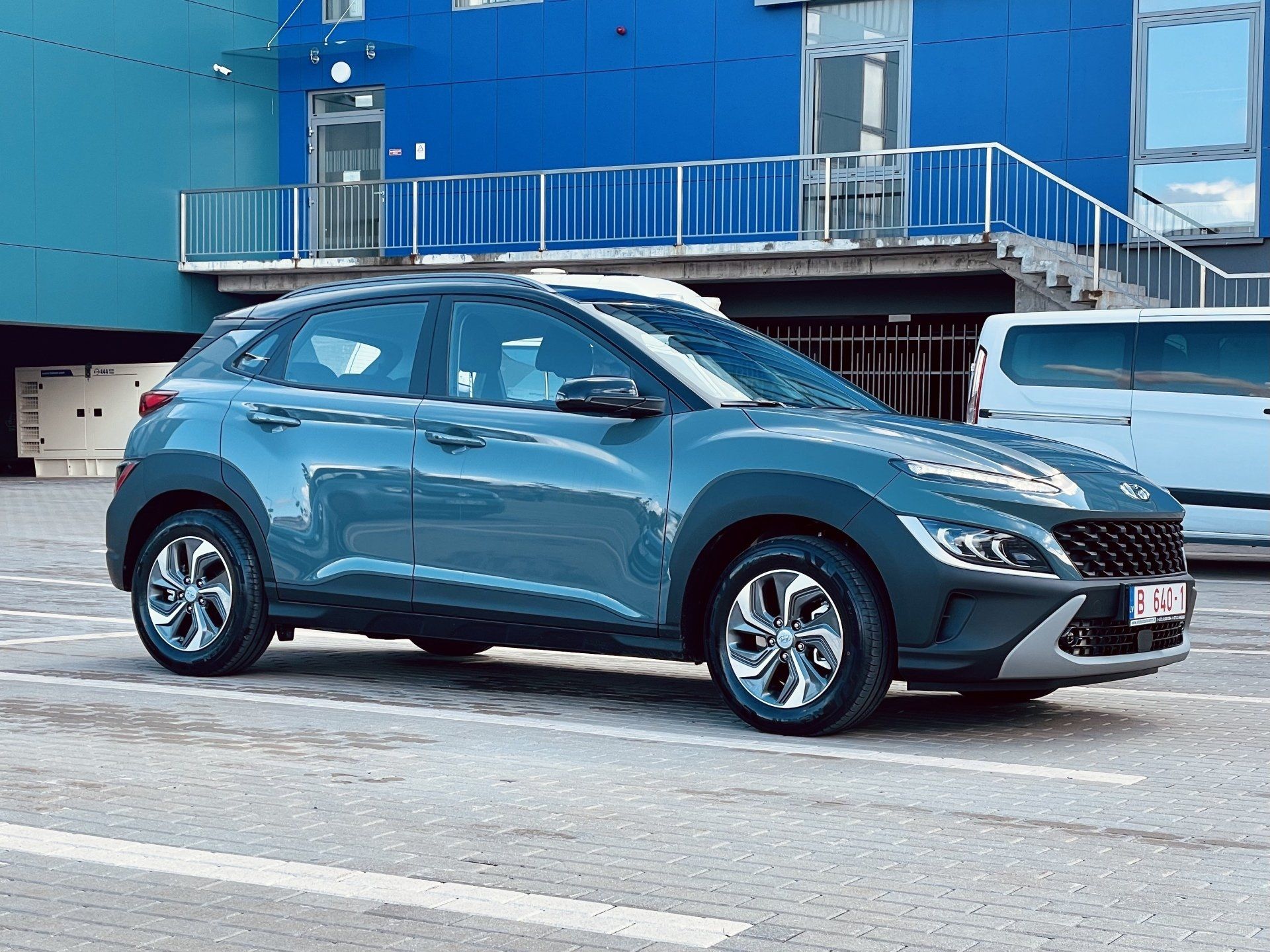 Zila automašīna ir novietota stāvlaukumā pie zilas ēkas.