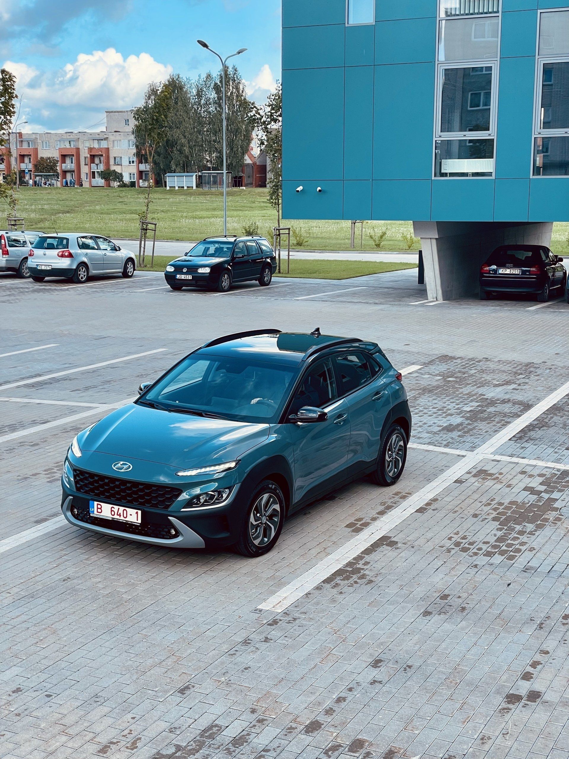 Zila automašīna ir novietota stāvlaukumā pie zilas ēkas.